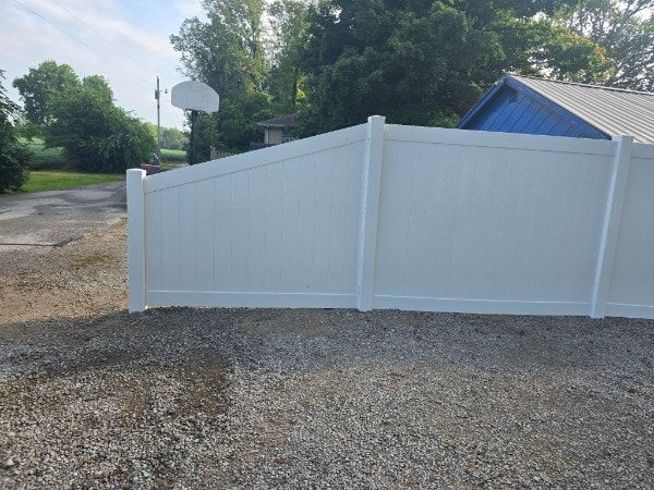 White vinyl privacy fence on a sloped driveway